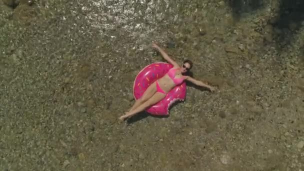 空中トップダウンかわいいブルネットは 水を通して広がった腕を持つドーナツフローティーに横たわっています 暑い夏の日に地元の川でくつろぐ気楽な女性 休暇を楽しむ女性観光客 — ストック動画
