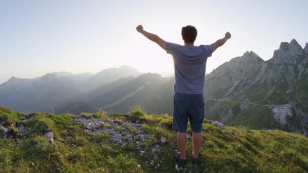 スローモーションレンズフレア 黄金の夏の夕日に岩山の上に腕を伸ばす陽気な若者 ハイカーは山頂に到達し 見事な山の風景の上に腕を上げる — ストック動画