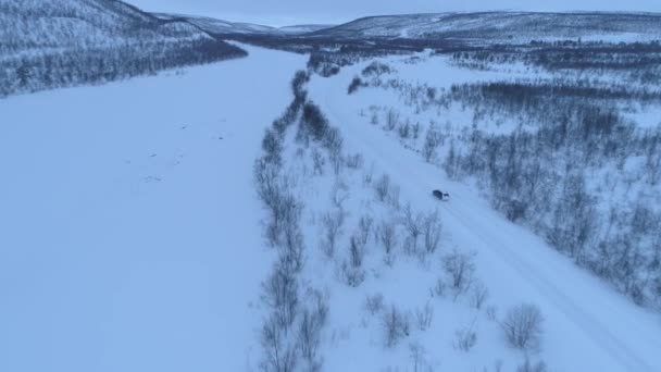 在森林雪山底部风景秀丽的乡村公路上行驶的汽车上方 穿越芬兰拉普兰的公路旅行 汽车穿越寒冬荒野 — 图库视频影像