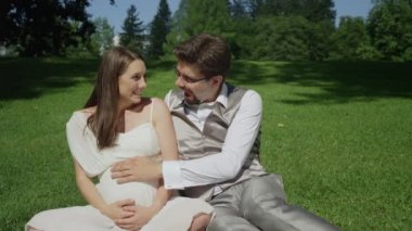 Slow Motion Loving çift park zemin de oturup bebek tekme hissediyorum. Yakında veliler güzel bir öğleden sonra açık havada hamilelik zevk olmak. Yeni evliler hamile göbek okşama doğmamış çocuk tekme hissediyorum