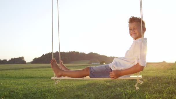 Slow Motion Closeup Smiling Young Boy Swings Relaxed Wood Swing — Vídeo de Stock