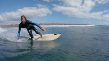 SLOW MOTION CLOSE UP: Male surfer riding blue breaking waves on a sunny day. Focused surfer carving wave and making sharp turn on his surfboard in awesome Fuerteventura. Young man having fun surfing.