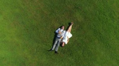 Aerial Top Down: Mutlu genç çift yaz günü çimenlerde yatıyordu. Düğünden sonra güneşli parkta dinlenen karı koca yeni evliler. Genç adam ve hamile kadın yalan ve el ele tutuşarak, bir bebek bekliyor