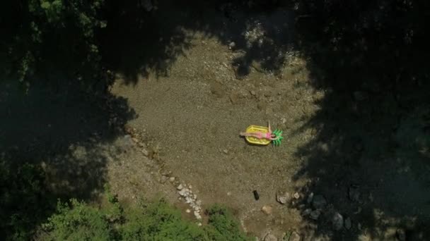 AÉRIEN Jeune femme allongée sur une flottille d'ananas les bras tendus, glissant sur l'eau pendant que son chien explore le sol de la rivière. Couché touriste et animal de compagnie prendre un peu de temps libre dans le grand air .