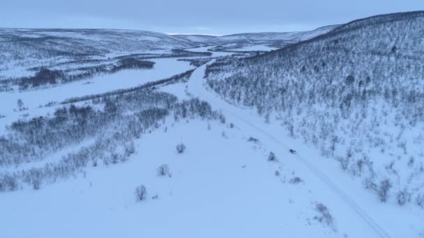 森林の雪山の底に風光明媚な田舎の高速道路を運転する車の上を飛ぶ フィンランドのラップランドを横断するロードトリップの人々 ウィントリーの荒野を旅する自動車 — ストック動画