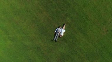 Aerial Top Down: Mutlu genç çift yaz günü çimenlerde yatıyordu. Düğünden sonra güneşli parkta dinlenen karı koca yeni evliler. Genç adam ve hamile kadın yalan ve el ele tutuşarak, bir bebek bekliyor