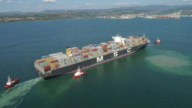 Koper, Slovenya - 7 Haziran 2017 Hava: Vinçlerle dolu bir tersaneye yaklaşan büyük uluslararası konteyner gemisi. Güneşli bahar öğleden sonra mesafe limana doğru sürüklenen yük gemisi