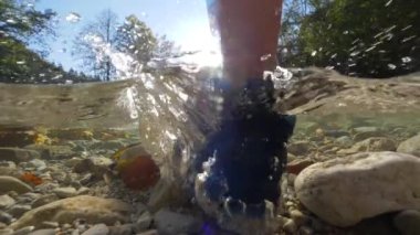 Yarım, Close Up Tanınmayan kadın trekker sığ sularda yürüyüş spor ayakkabıları giyen ve kamera dan uzağa bakan. Doğada güzel güneşli sonbahar günü, kadın berrak nehir aşağı yürüyor