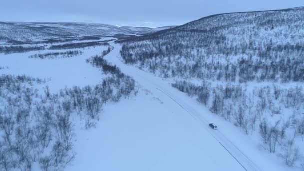 森林の雪山の底に風光明媚な田舎の高速道路を運転する車の上を飛ぶ フィンランドのラップランドを横断するロードトリップの人々 ウィントリーの荒野を旅する自動車 — ストック動画