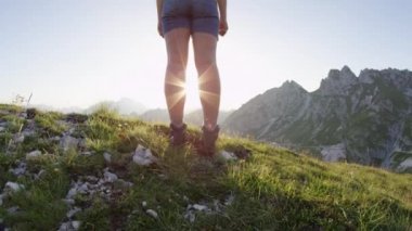 Slow Motion Close Up Lens Flare: Altın yaz gün batımında kayalık dağın tepesinde kollarını muzaffer bir şekilde kaldıran mutlu genç kadın. Gün doğumunda bir dağın tepesine ulaşırken yürüyüş kız kollarını uzanan