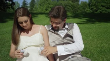 Slow Motion Happy çifti düğünlerinden hemen sonra doğmamış bebekleri ile oynuyor. Erkek ve kadın eğlenceli parmaklarına bebek ayakkabıları koyarak ve kadının sevimli bebek yumru üzerinde yürüme bir çocuk bekliyor.