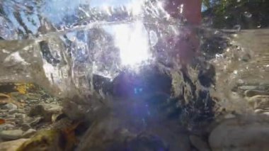 Yarım, Lens Flare: Bilinmeyen trekker sığ bir orman dere boyunca yürüyor. Temiz su sıçrayan ve tanınmaz bir kişi olarak köpüren soğuk nehir suyuna kayalık bir nehir yatağından aşağı doğru ayak basar.