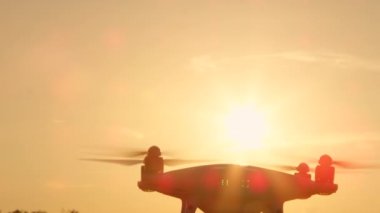 Yakın Çekim Lens Flare Siluet Küçük filme drone altın günbatımı gökyüzü üzerinde uçan. Altın ışıkta çekim eklenmiş kamera ile beyaz quadcopter drone. Gündoğumu gökyüzünde uçan Quadrocopter helikopter