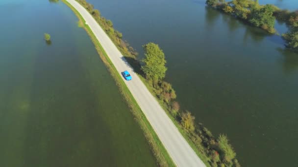 恐ろしい洪水の後 秋の自然を乾燥して走る狭い道路を走る青い車の上を飛んで追う 自然災害の余波でハッチバッククルージングの人々 — ストック動画