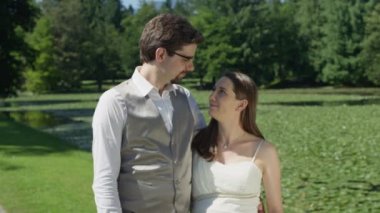SLOW MOTION CLOSE UP: Loving husband with arms wrapped around his wife, gives her gentle kiss on forehead. Devoted young couple embrace and smile at the camera. Man tenderly caresses wife's baby bump
