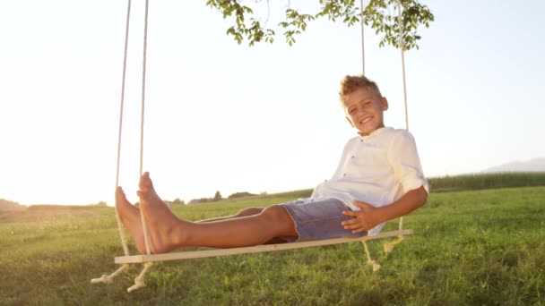 Медленное Приближение Счастливый Мальчик Сидит Расслабленный Качелях Летнем Закате Вечером — стоковое видео