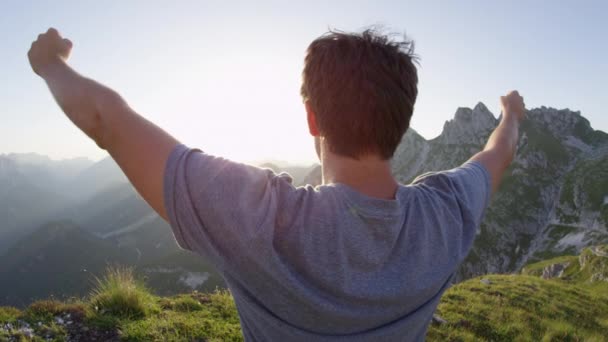 クローズアップレンズフレア 山頂に立つ興奮した若者 息をのむような夏の夕日で勝利に腕を伸ばす 急な登山を祝い 景色を楽しむ未知のハイカー — ストック動画