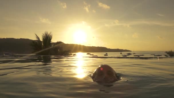 スローモーション クローズアップ レンズフレア 気楽な女性は 日没時に壮大なインフィニティプールから立ち上がります 若い女性観光客は 黄金の太陽の光がエキゾチックなビーチに輝くようにきらめくプールの水から出てくる — ストック動画