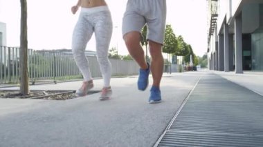 Güneşli şehir sokaklarını birlikte çalışan genç bir beyaz çift. Tanınmayan sarışın kadın ve gömleksiz adam yeşil avenue doğru eğimli bir kaldırım kadar güneşli sabahı kentsel şehirde jog.