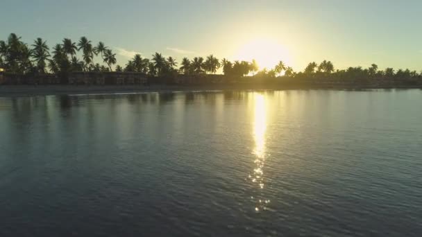 息をのむ美しい熱帯の島とリゾートに輝く夕暮れに向かって空中 レンズフレア 飛んで 太平洋諸島のリモートのビーチに面したリゾートに近づいて穏やかな海の壮観なショット — ストック動画