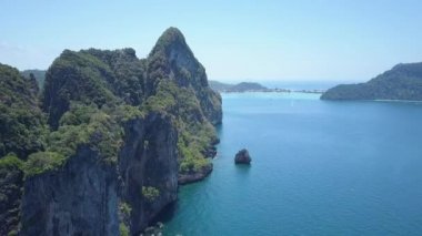 Hava: güneşli turist beach Tayland yakınındaki gür tropikal yeşil kaplı büyük kalker uçurum boyunca uçan. Büyük karstik oluşumu uzak beach yaklaşan mavi okyanus dalgaları üzerinde yükselir.