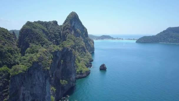 在泰国阳光明媚的旅游海滩附近 沿着巨大的石灰岩悬崖飞行 覆盖着郁郁葱葱的热带植物 巨大的岩溶地层在接近遥远海滩的蓝色海浪中翱翔 — 图库视频影像