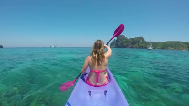 素晴らしい休暇上のアクティブな白人の女の子は 見事な砂浜に向かって彼女のカヤックをパドル 鋭い岩の島を過ぎたゴージャスなターコイズブルーの海の水でビキニのパドリングで女性の観光客 — ストック動画