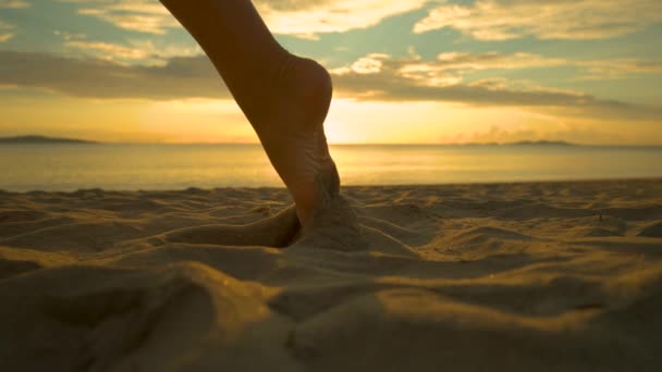 スローモーション クローズアップ レンズフレア 裸足の女性ジョガーは 日没時に暖かい夕方の空気の中で砂の道を残します 女性が日当たりの良い熱帯のビーチに沿って走るように 砂の黄金の斑点が空中で高く飛ぶ — ストック動画