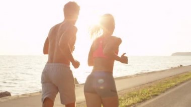 Genç erkek arkadaşı ve kız arkadaşı birlikte güneşli sahilde jogging. Huzurlu okyanus boyunca sportif Tarih jog üzerinde kadın aktif adam. Yaz aylarında açık havada egzersiz mutlu çift.