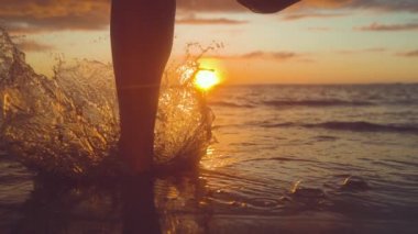 Yavaş Hareket, Close Up, Copy Space: Tanınmayan kadın turist pastoral egzotik gün batımında sığ okyanus suyuna çalışır. Tropikal plajda kaygısız kız altın gün doğumunda ferahlatıcı denize çalışır.