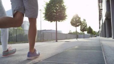 Güneşli şehir sokaklarını birlikte çalışan genç bir beyaz çift. Tanınmayan sarışın kadın ve gömleksiz adam yeşil avenue doğru eğimli bir kaldırım kadar güneşli sabahı kentsel şehirde jog.