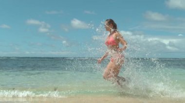 Slow Motion: Pembe mayo giyen genç beyaz kadın mükemmel yaz gününde sığ okyanus sularında koşuyor. Serin tatil çalışan mutlu kız çalışan ve egzotik plajda beyaz kumlu plaj da atlama.