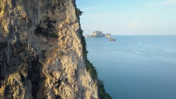 在泰国阳光明媚的旅游海滩附近 沿着巨大的石灰岩悬崖飞行 覆盖着郁郁葱葱的热带植物 巨大的岩溶地层在接近遥远海滩的蓝色海浪中翱翔 — 图库视频影像