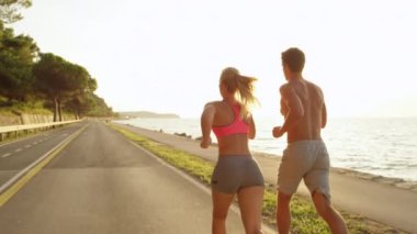 Genç erkek arkadaşı ve kız arkadaşı birlikte güneşli sahilde jogging. Huzurlu okyanus boyunca sportif Tarih jog üzerinde kadın aktif adam. Yaz aylarında açık havada egzersiz mutlu çift.
