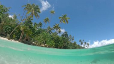 Yarım Sualtı: Onu çevreleyen berrak mavi su dan kumlu kıyı şeridi üzerinde gökyüzünün büyüleyici görünümü. Fiji adasında sualtı dünyasını keşfetmek. Okyanus tabanında parlayan deniz yüzeyi gibi cam