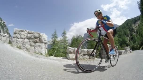 激しい山岳レース中に彼のクールな道路の自転車のペダルを踏んで運動若い男性 日当たりの良い山のプロロードサイクリストトレーニング 夏の自然の中で美しい自転車に乗る — ストック動画