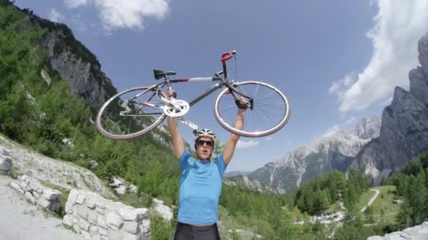 欣喜若狂的年轻自行车运动员在美丽的山上举起他的公路自行车 快乐的运动员自豪地举起他的自行车头顶上华丽的山区景观和晴朗的蓝天包围 慢镜头 — 图库视频影像