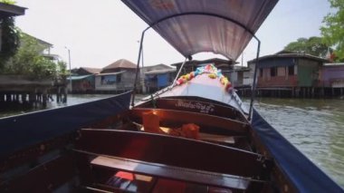 Düşük Açı: Çürüyen ahşap evlerin yanından geçen nehir kanallarının karmaşık ağı. Turist su taksi kirli Chao Phraya nehri üzerinde eski kulübeler geçmiş döner. Longtail tekne daha küçük bir kanal haline sola dönüyor.