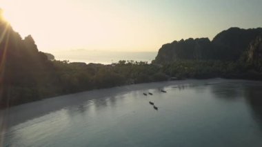 Hava: güneşli turist beach Tayland yakınındaki gür tropikal yeşil kaplı büyük kalker uçurum boyunca uçan. Büyük karstik oluşumu uzak beach yaklaşan mavi okyanus dalgaları üzerinde yükselir.