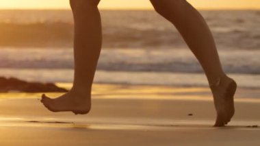Yavaş Hareket, Lens Flare: Bir yaz akşamı ıslak kum üzerinde yalınayak çalışan tanınmayan kadın. Okyanus dalgaları ıslak kumlu kıyıya ulaşmak gibi güneşli bir tropik plajda koşu ayak bileği bileziği ile Aktif kadın