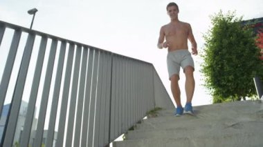 Yavaş Hareket, Düşük Açı: Güneşli şehir sokaklarında koşarak maraton için sert erkek eğitim uygun. Atletik erkek koşu ve maraton gömleksiz için eğitim. Beton merdivenlerden aşağı koşu neşeli sporcu