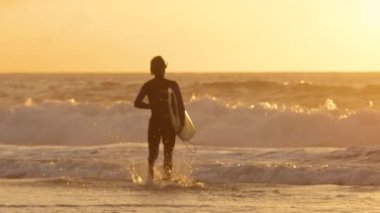 Yavaş Hareket: Altın gün doğumunda dalgalar kırma sörf suya çalışan genç sörfçü. Tasasız erkek surfboarder güzel yaz gün batımında onun serin sörf tahtası üzerinde dalgalar binmek için okyanusa koşu.