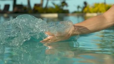 Slow Motion, Close Up: Oyuncu kadın turist havuz suyu ile elini sürükler ve serin bir dalga oluşturur. Yaz tatilinde tanınmayan kadın güneşli okyanus kıyısındaki tatil beldesinde kristal berraklığında havuzda oynuyor.