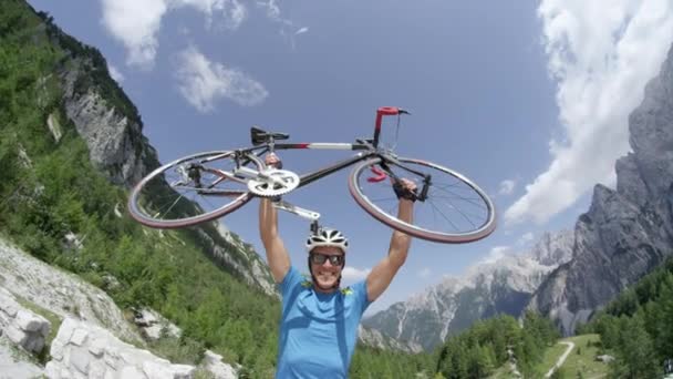スローモーションクローズアップローアングル 彼の頭の上に彼の自転車を上げることによってトップに到達を祝う興奮若い男性サイクリスト 勝利のバイカーは 美しい夏の日に彼の目標を達成することに成功しました — ストック動画