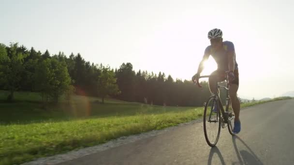 コピー スペース レンズフレア プロ男性道のバイカーは彼の自転車で日当たりの良いクルーズを楽しんでします 日当たりの良い春の田園地帯を通ってプロ自転車ロードレースのレースのサングラスと活発な男性 — ストック動画