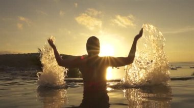 Slow Motion, Close Up, Lens Flare: Plaj serin bir görünümü ile sonsuzluk havuzunda rahatlatıcı eğlenceli kadın elleriyle camsı havuz suyu sıçratıyor. Neşeli kız gün batımında ellerini havuzdan kaldırıyor.