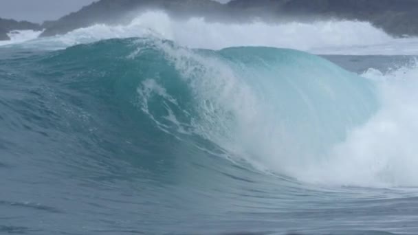 スローモーション クローズアップ 美しいバレル波は 岩の黒いビーチの上に飛び散る 無限の青い海から来る一連の発泡管の波によって霧の朝に洗われている荒い海岸線 — ストック動画