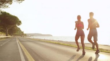 Yavaş Hareket, Lens Flare, Copy Space: Güneş ışınları kadar sırılsıklam tatil de tanınmayan jogging çift. Okyanusa bakan güzel güneşli bir yolda koşan sağlıklı bir çift. Rahatlatıcı akşam koşu.