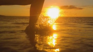 Yavaş Hareket, Close Up, Lens Flare: Tasasız kadın altın gün batımında sığ okyanus suyunda yalınayak çalışır. Genç kadın gezgin güzel yaz sabahı koşarak ve denize sıçrayarak gevşer.