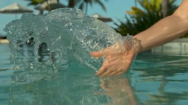 Yavaş Hareket, Yakın Çekim: Tanınmayan kadın turist elini sakin havuz suyuna sürükler ve bir dalgalanma yaratır. Kafkas kadın Fiji Adaları egzotik bir otel tesisi çarpıcı havuzda oynuyor.